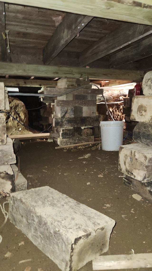 Stacks of timber cribbing under the floor beams, with a white bucket on the dirt floor